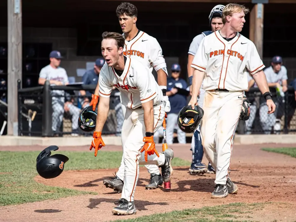 Princeton baseball player in a white jersey celebrates and runs into the field.