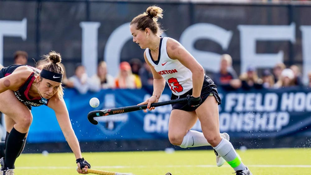 A field hockey player moves across the field with ball in midair.