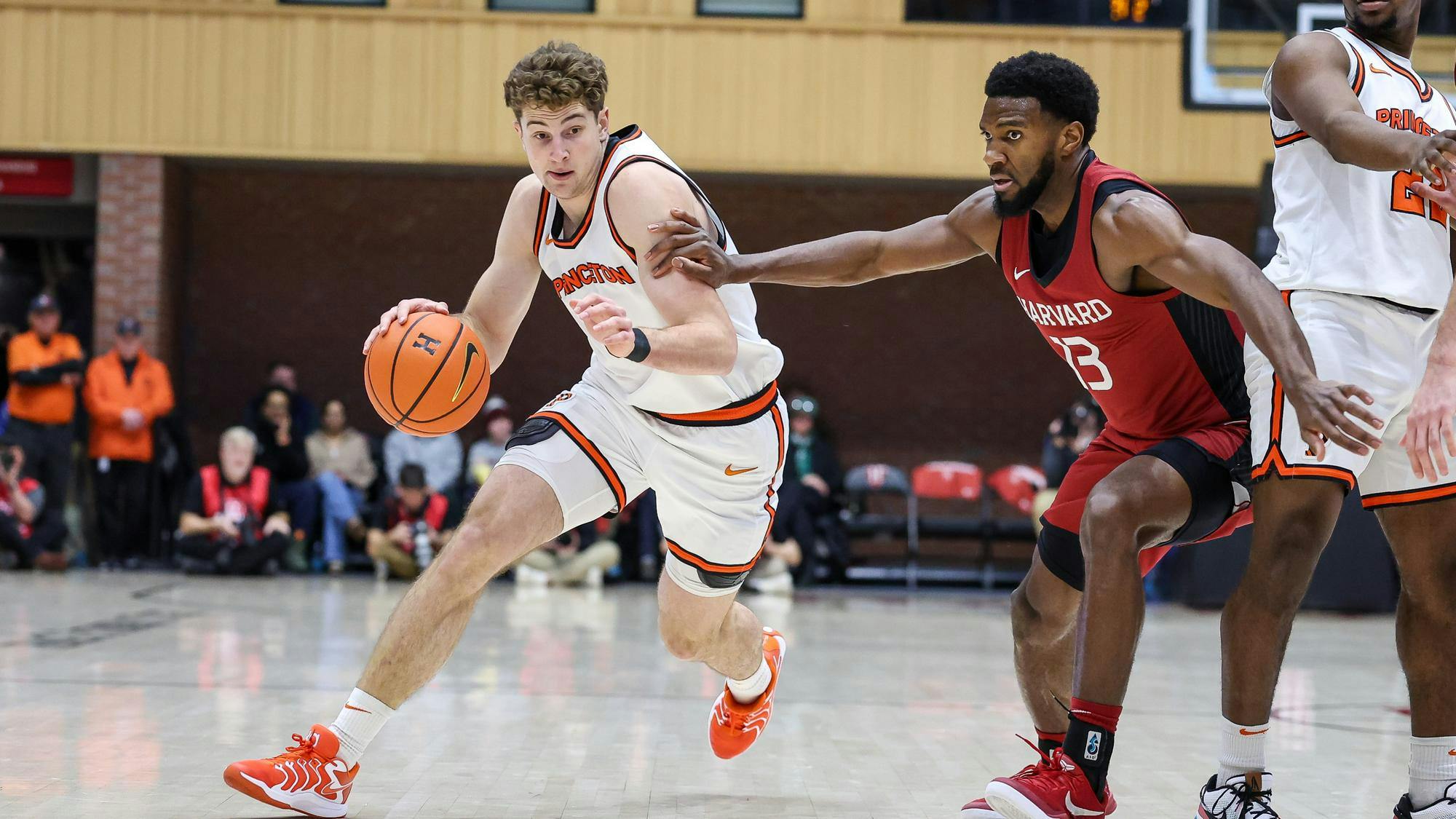 Caden Pierce in white Princeton jersey dribbles basketball by Harvard player in crimson jersey