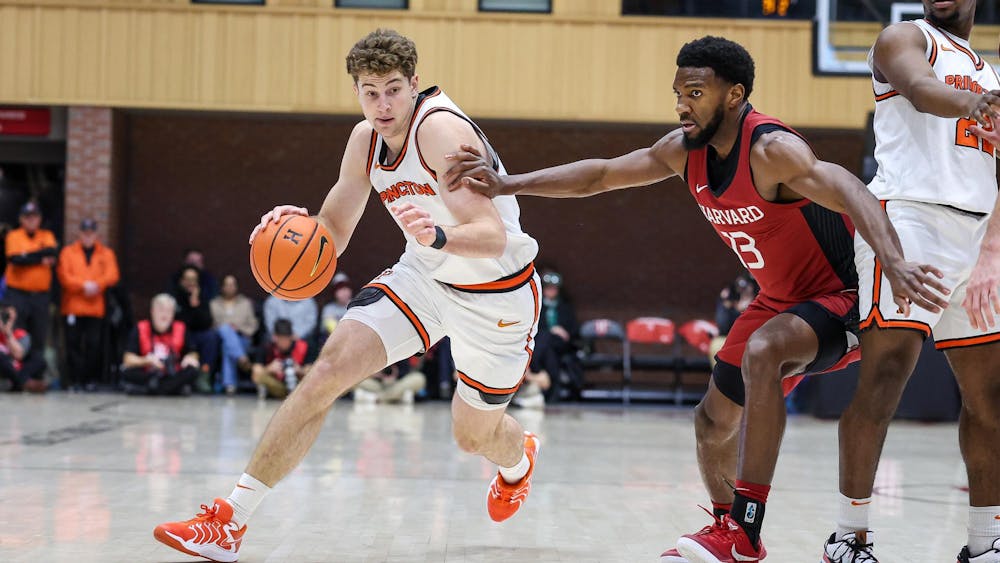 Caden Pierce in white Princeton jersey dribbles basketball by Harvard player in crimson jersey