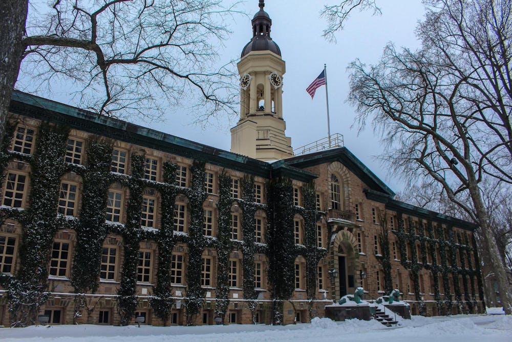 Brown brick building covered in green ivy in the snow, with clocktower and American flag on top.