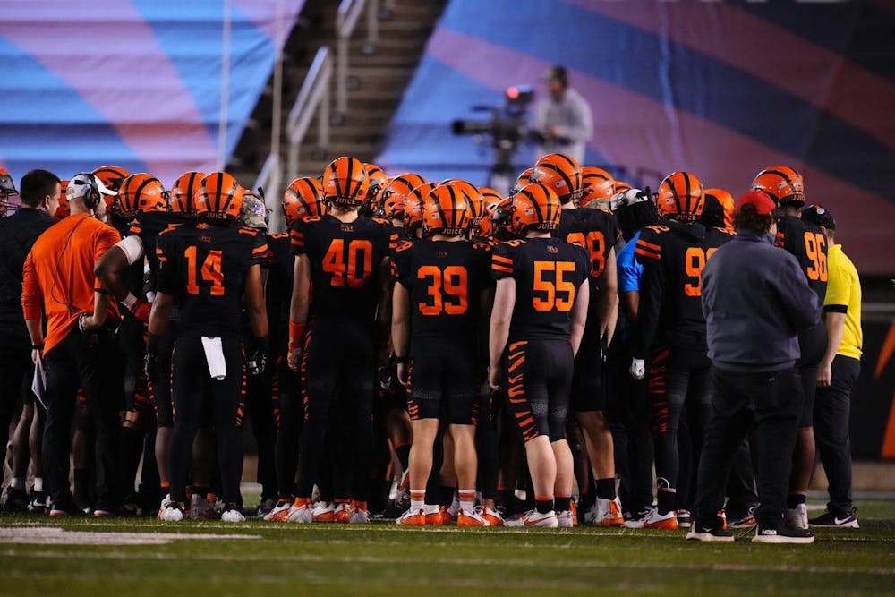 A group of men standing on a football field in orange and black attire. 