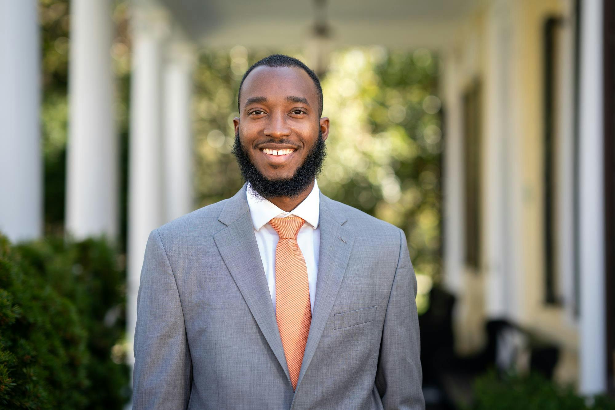 African American person in grey suit with orange tie, standing in front of building