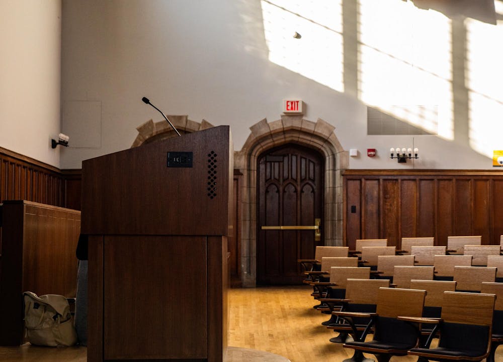 A lectern and a bunch of chairs and a door.  Brown background with sunlight streaming in.