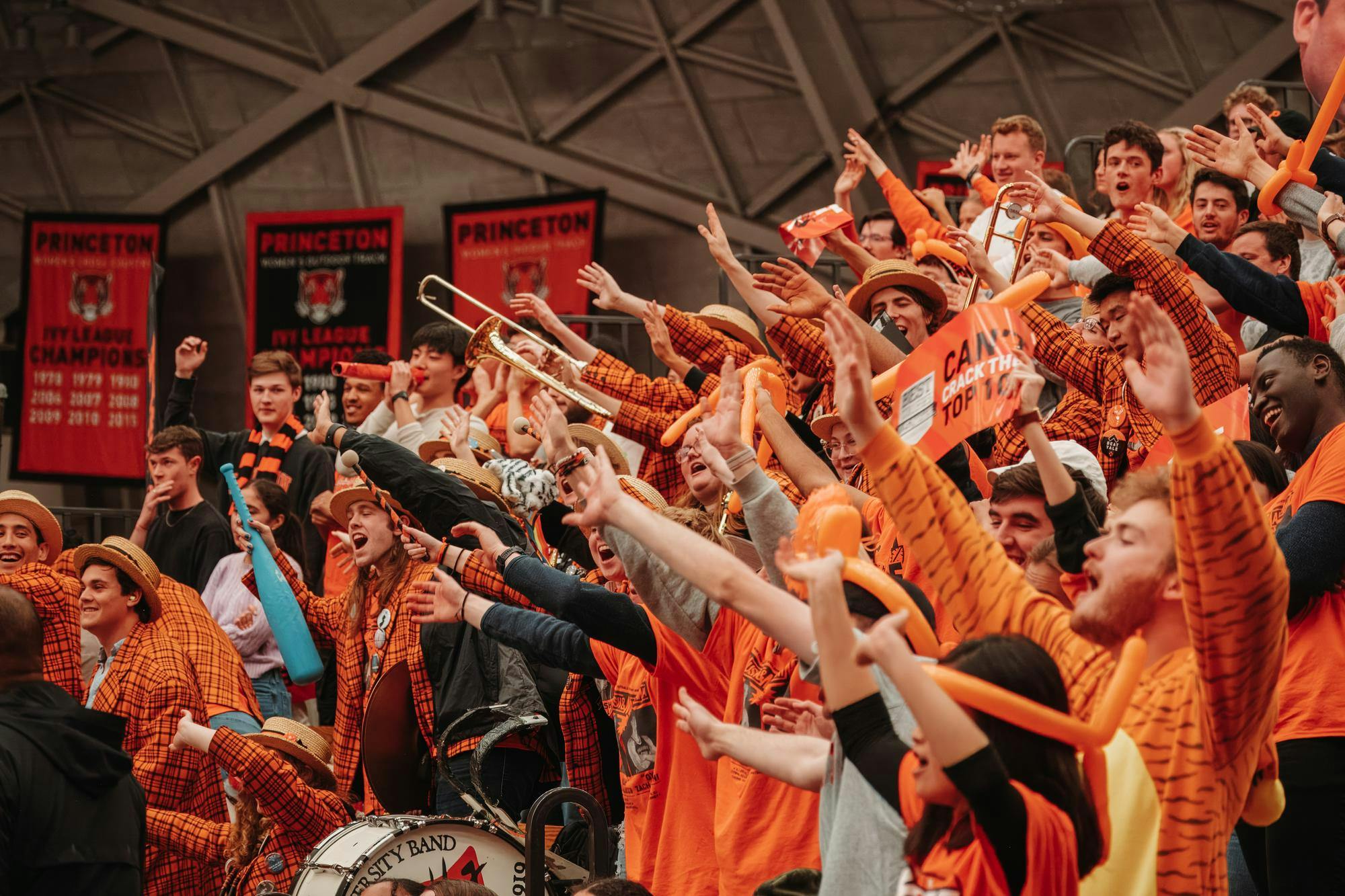 Crowd of students with hands raised cheering in bright orange gear.