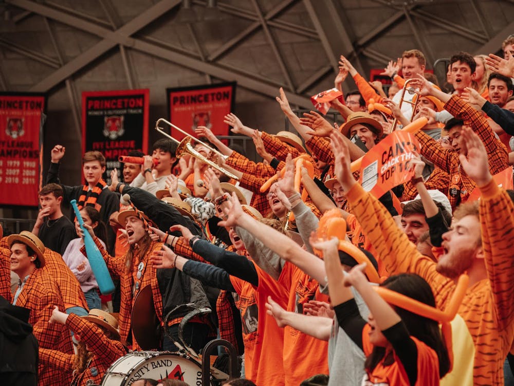 Crowd of students with hands raised cheering in bright orange gear.