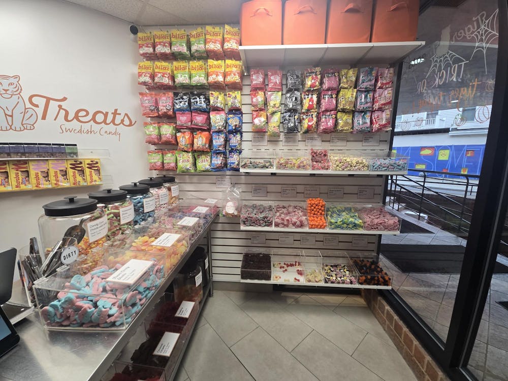 Multicolored bags of candy are hanging on a white wall. There is a Tiger Treats sign in orange script font on the adjacent white wall.