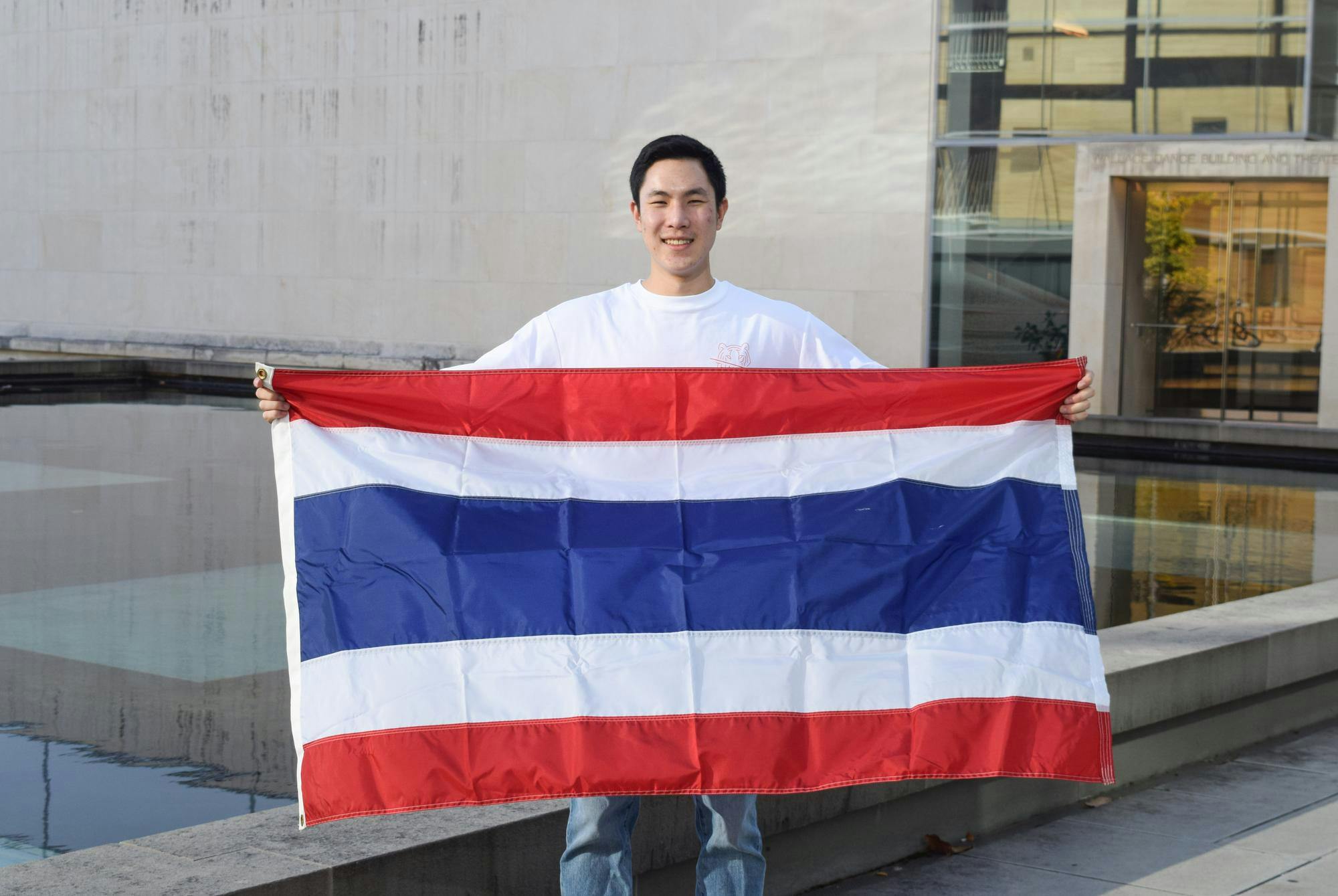Student stands in the center, holding the flag of Thailand.