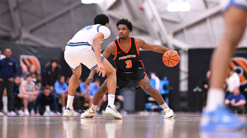 A player in a black and orange No. 3 jersey dribbles a basketball while a defender in a white and light blue jersey guards him.