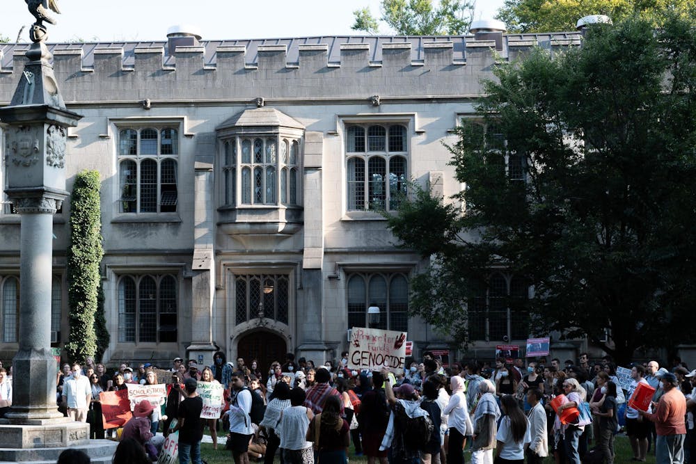 People stand holding signs in a green courtyard. One prominent sign says "Princeton funds Genocide" and has red handprints on it. 