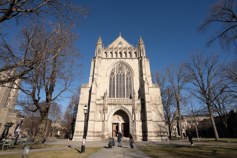 A gray chapel with arched doorways, framed by trees against a blue sky