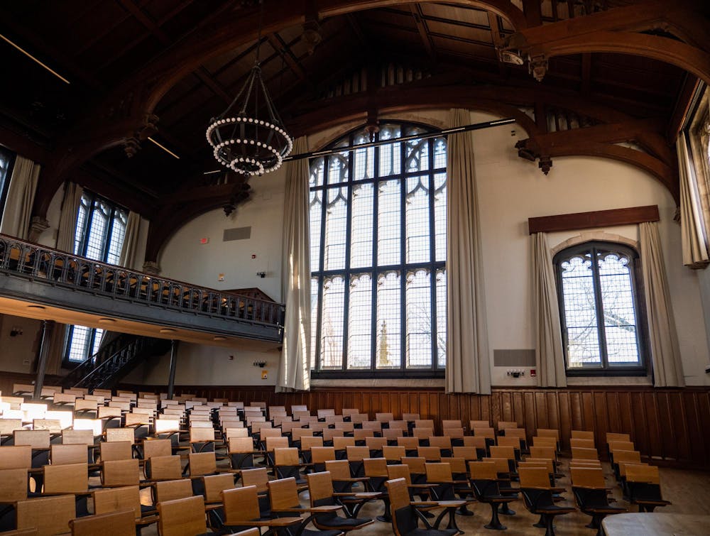 A large room filled with wooden chairs is backed by sweeping windows. A chandelier hangs from the ceiling.