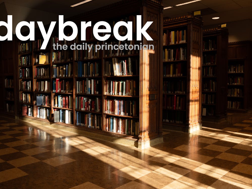 Photo of wooden library bookshelves, a checkerboard wooden floor, light from windows shines onto them. In the top left, a logo that says "daybreak: the daily princetonian"