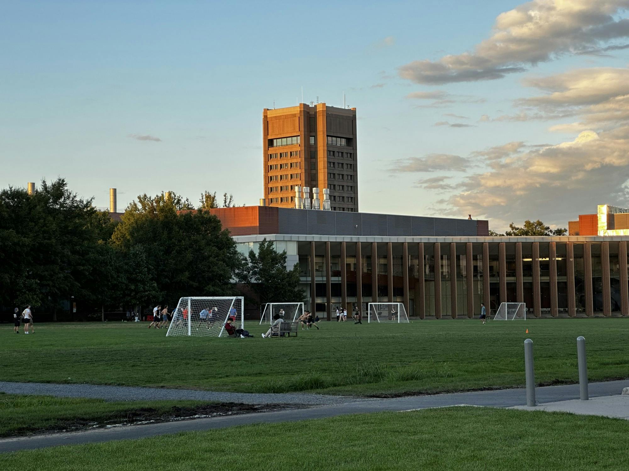 A few students on a soccer field playing frisbee, with a tall building in the background.