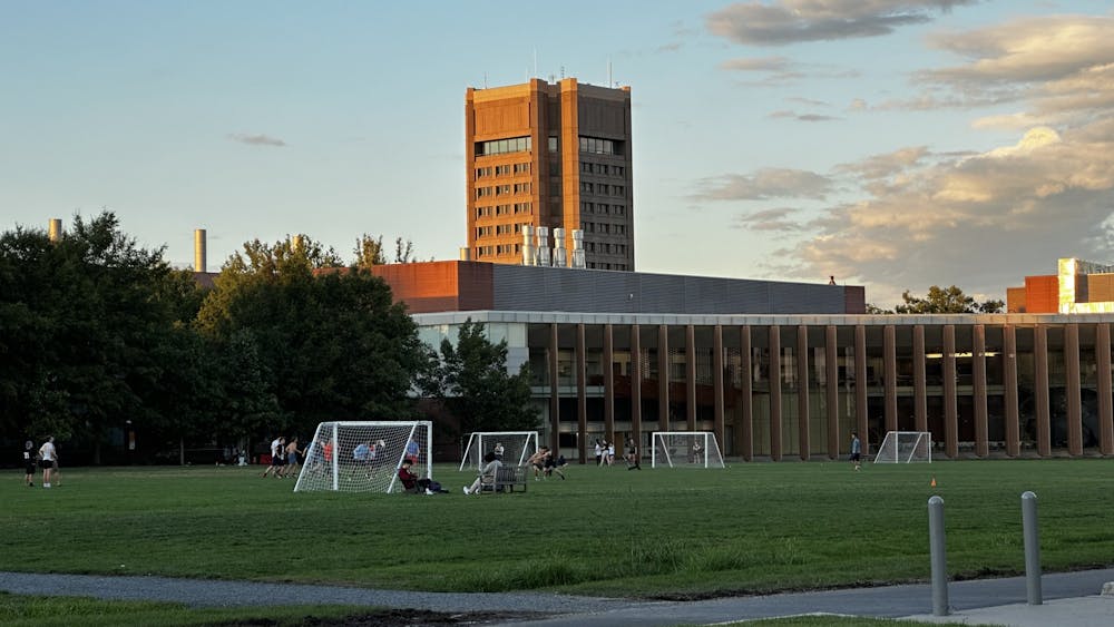 A few students on a soccer field playing frisbee, with a tall building in the background.
