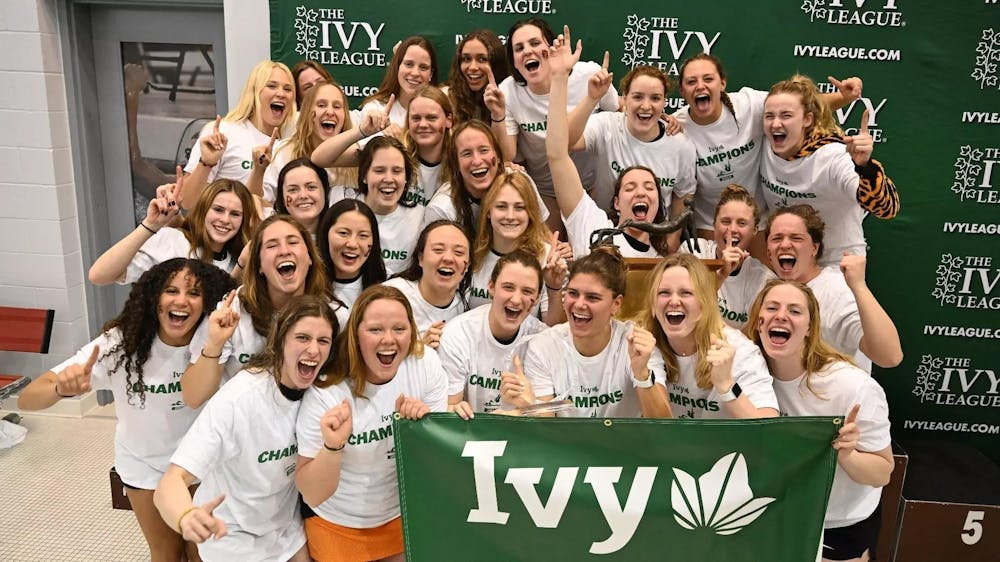 A group of women in front of a green backdrop, holding onto banner with words, “Ivy.”
