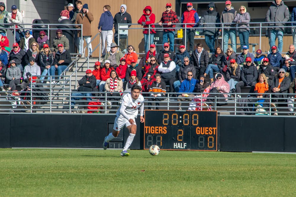 A Princeton player runs toward the ball with a crowd and scoreboard in the background.