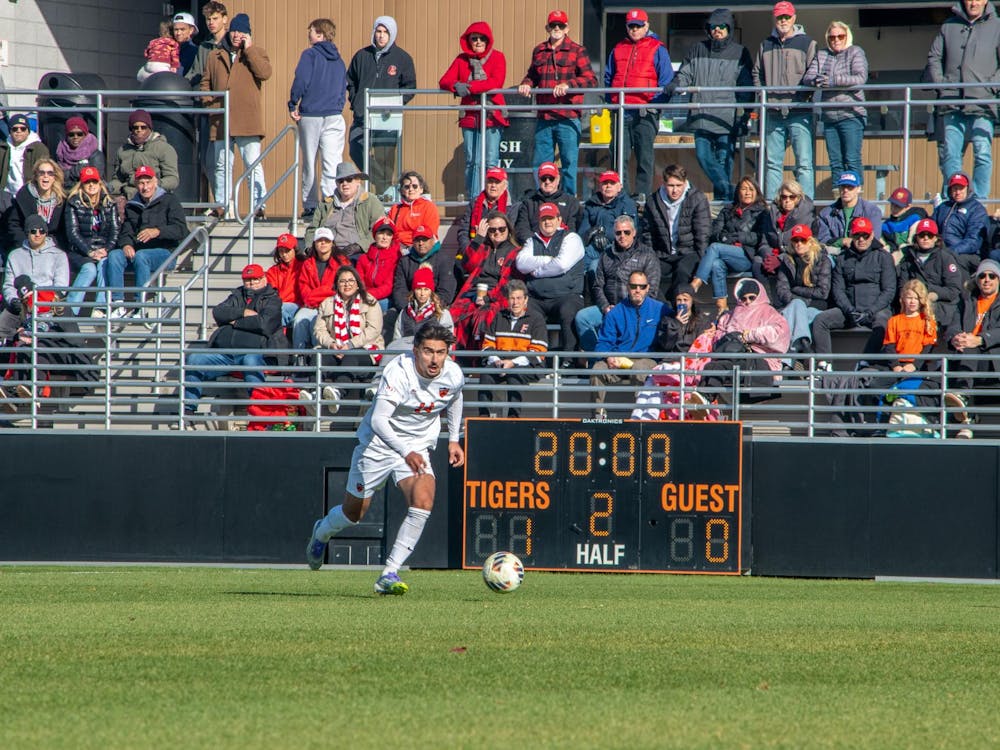 A Princeton player runs toward the ball with a crowd and scoreboard in the background.