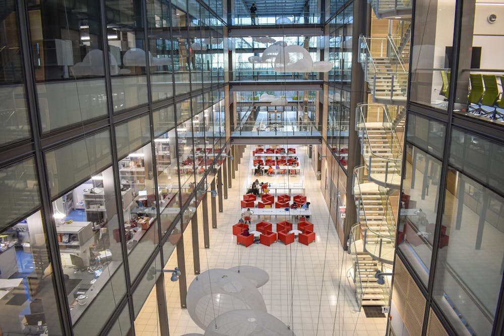 Interior of large multistory glass building with red seating in the center, and white hanging lights above.