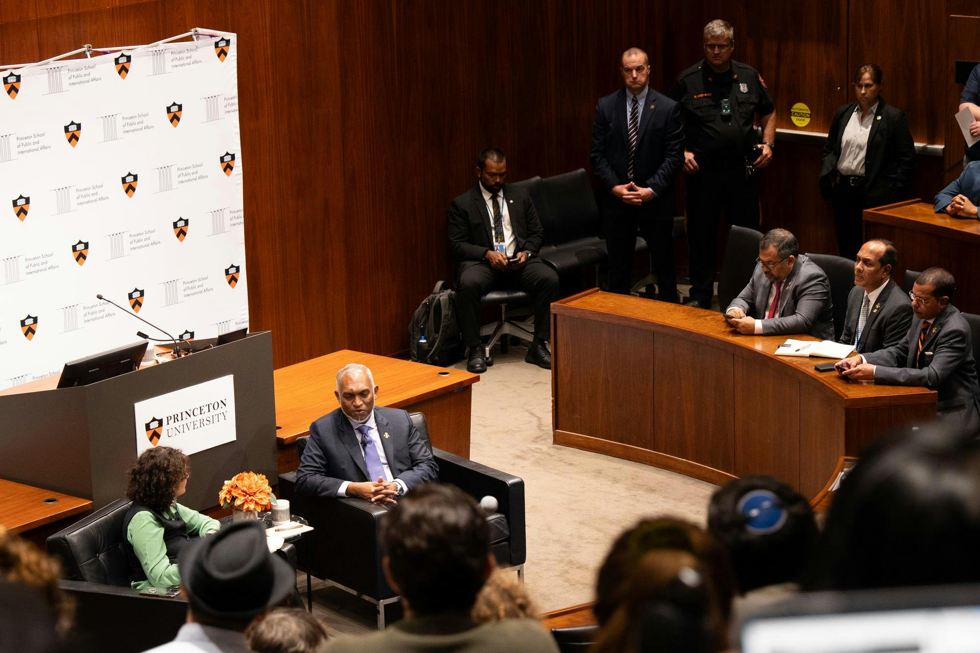 Two people sitting in the center of a room in discussion, with people in raised seats sitting around them.