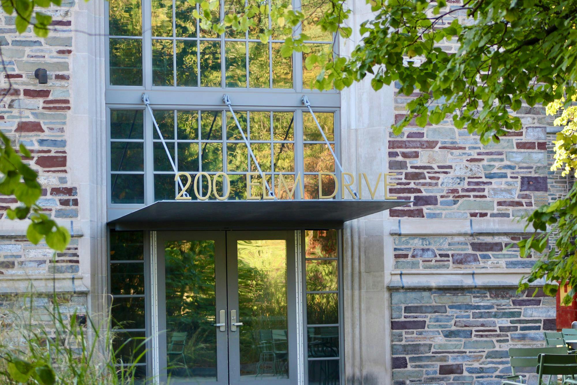 A brick building with a modern entrance in the middle, surrounded by greenery. 