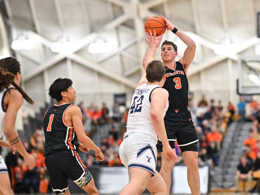 A man shoots a basketball over the outstretched arms of the defender as the crowd watches on.