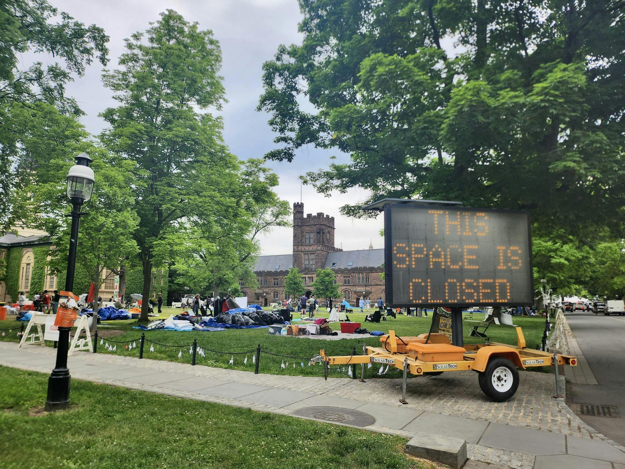 A grassy field with various people and piles of supplies. A large electronic billboard reads "This space is closed."