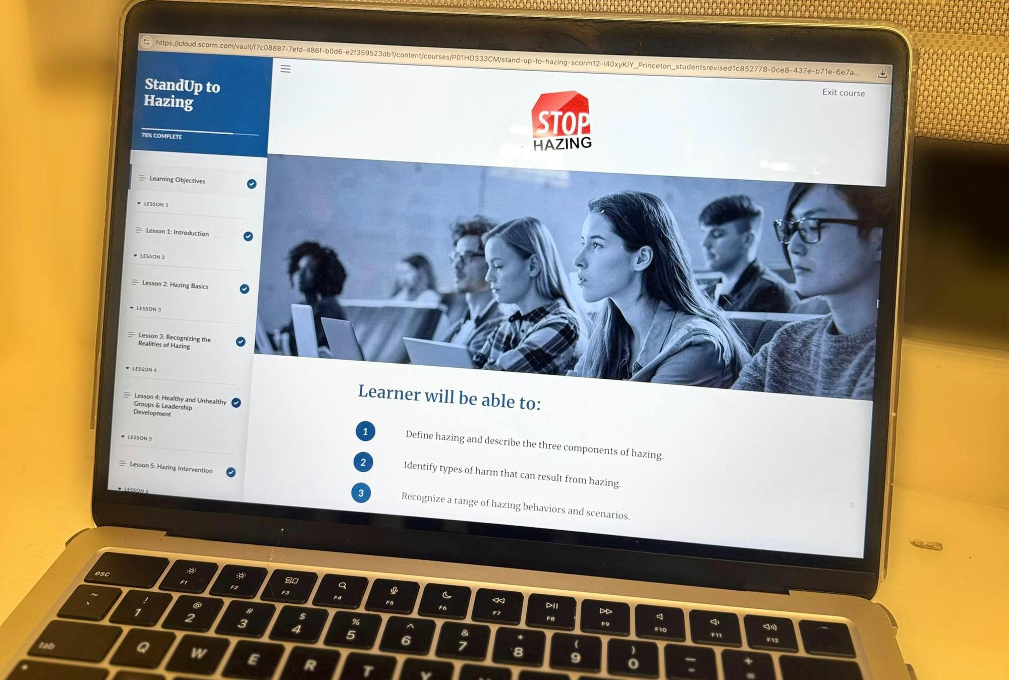 An Image of a laptop with the “StandUp to Hazing” course open. There is an image of students with a Stop Hazing logo on the screen. Below the image there are a list of learning expectations and there is a side bare containing a list of each lesson included in the course. 
