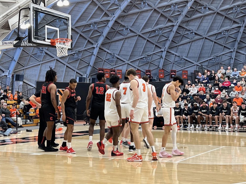 The Cornell (left) and Princeton (right) men's basketball teams stand under a basketball hoop.