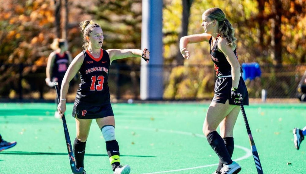 Two women wearing black jerseys playing field hockey