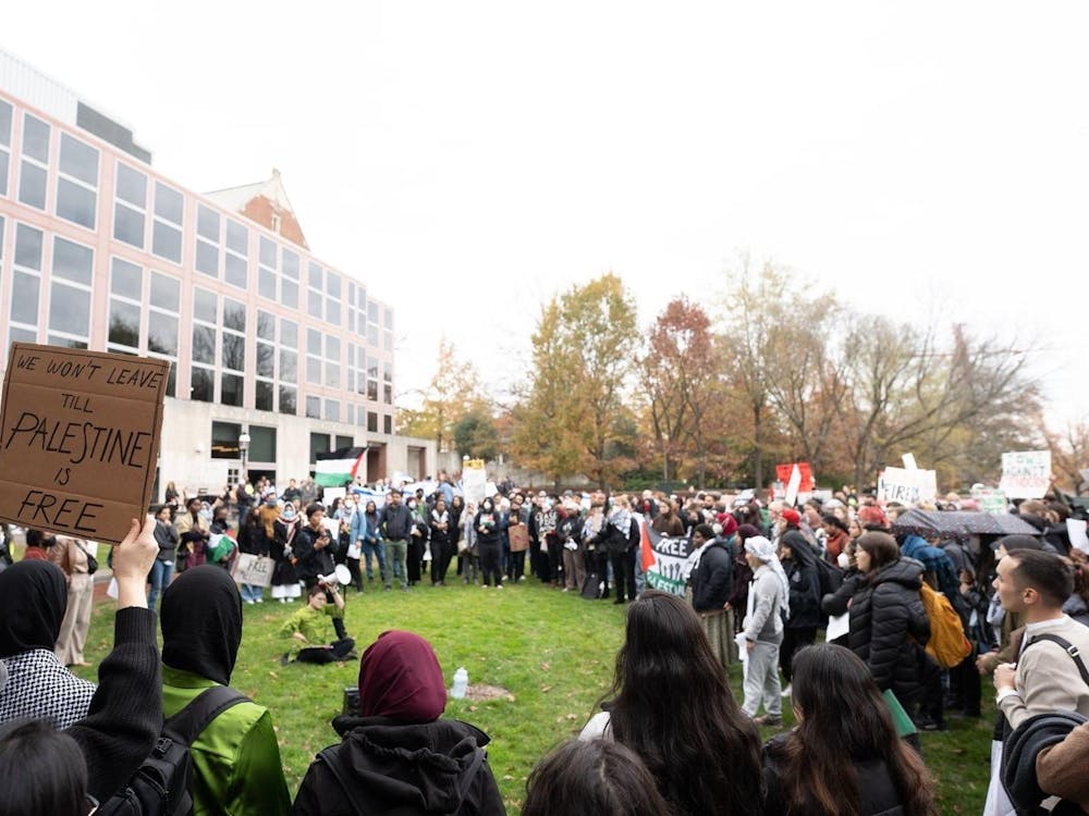 A group of students holding protest signs form a circle on a lawn.