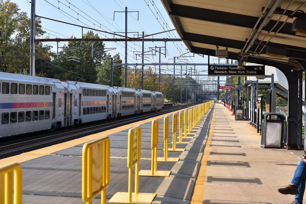 A gray NJTransit train exiting a station on a sunny day. A sign says "Tickets/Tunnel" and "Newark/New York Trains."