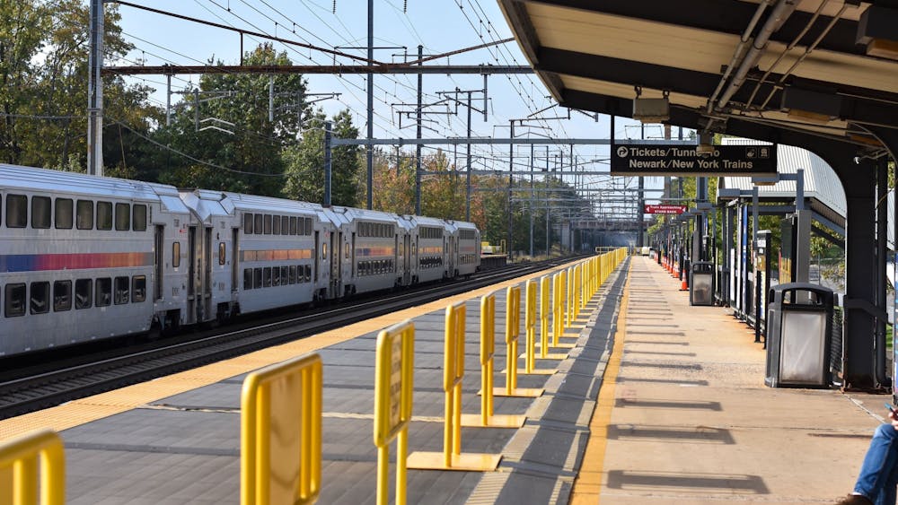 A gray NJTransit train exiting a station on a sunny day. A sign says "Tickets/Tunnel" and "Newark/New York Trains."
