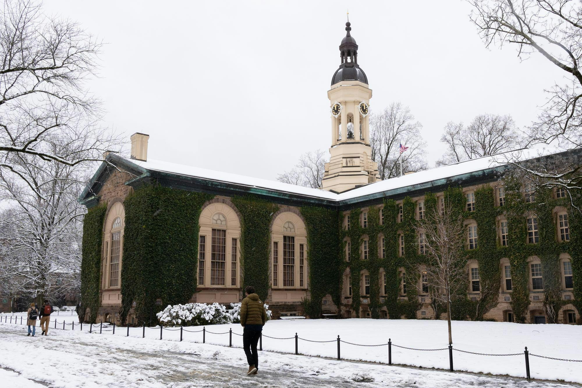 An ivy-covered building covered in snow on a winter day, with three students walking to the left.
