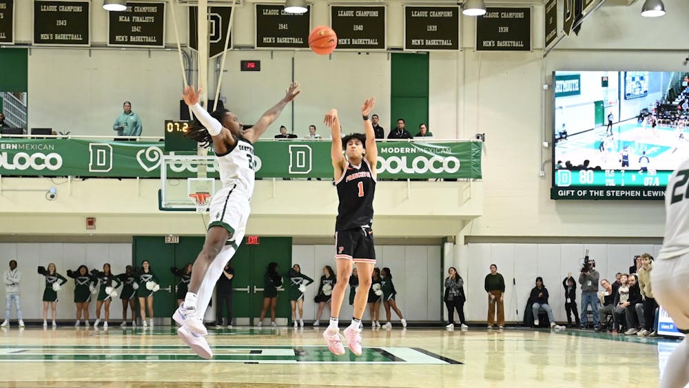 Xavian Lee in black uniform shoots three-pointer over Dartmouth player in white and green.