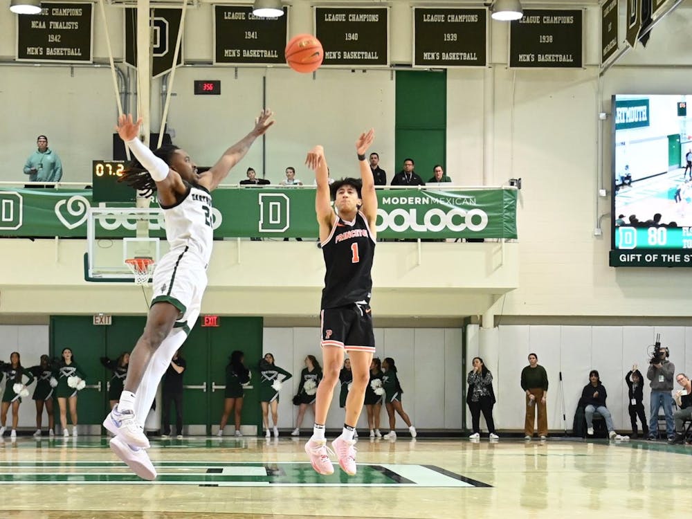 Xavian Lee in black uniform shoots three-pointer over Dartmouth player in white and green.
