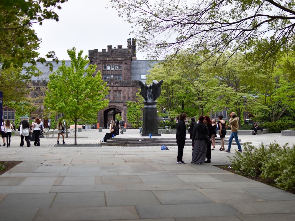 A courtyard on a sunny day with people milling, trees, and buildings in the background.