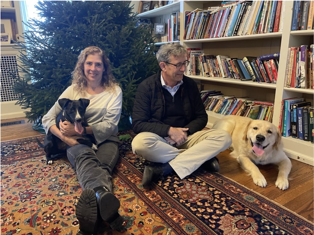 A woman sits on the left holding a black and white dog. On the far right is a golden retriever, laying on the floor next to a smiling man.