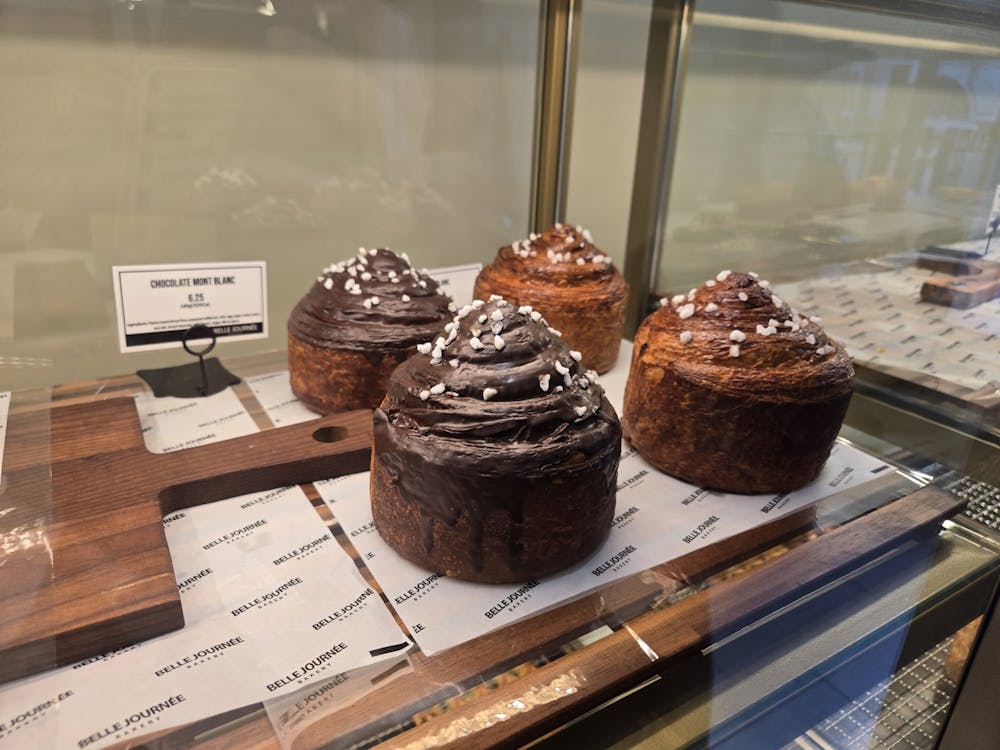 Four brown chocolate croissant pastries on a tray behind a glass display. 