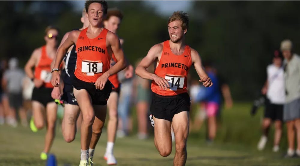 Two men wearing orange jerseys run alongside each other. 