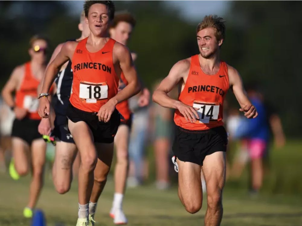 Two men wearing orange jerseys run alongside each other. 