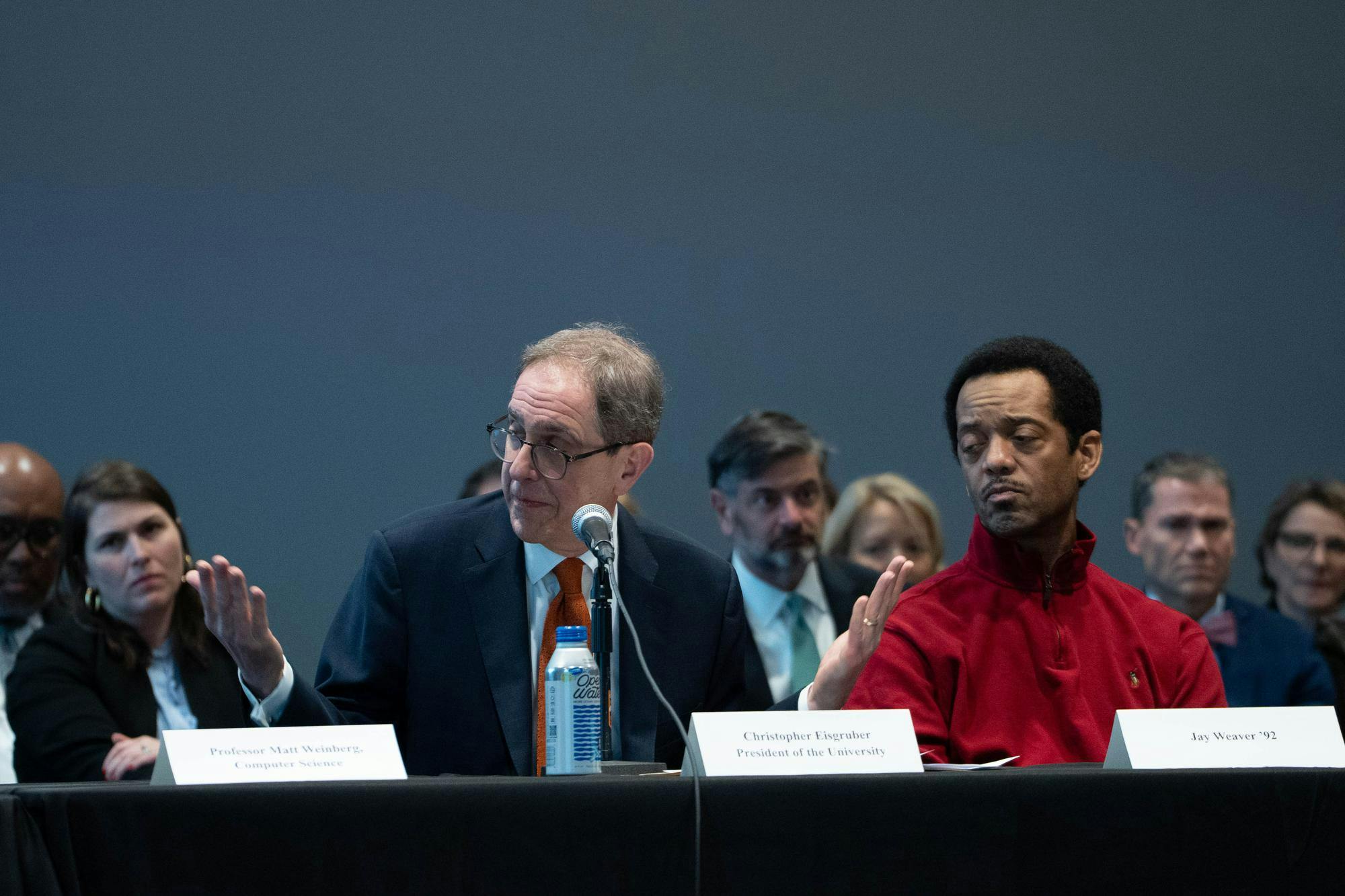 President Eisgruber sits at a table shrugging. 