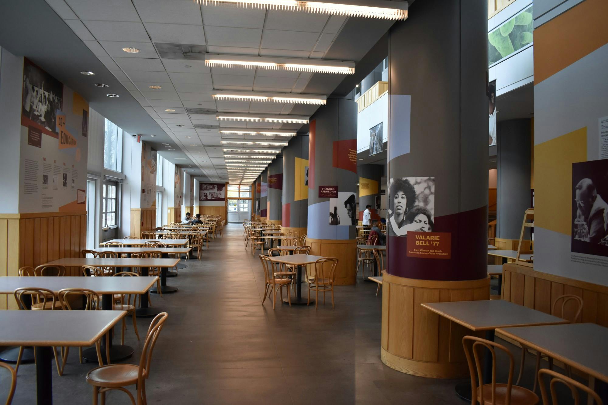 Room full of tables and chairs, with cement floors, and walls and pillars covered in colorful posters.