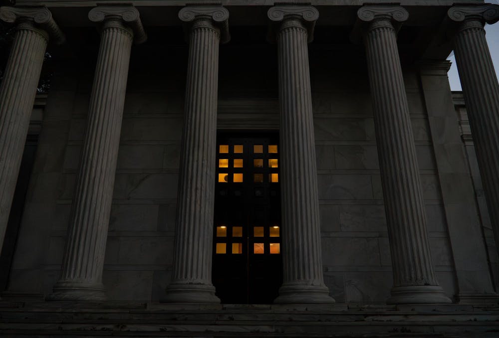 A photo of Whig Hall during dusk, with an orange glow behind the door's windows.