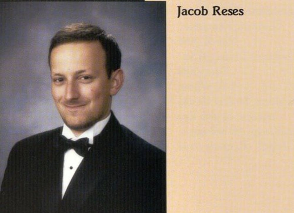 Man in a black and white tuxedo with a blue background, with black text reading "Jacob Reses" in front of a beige background.