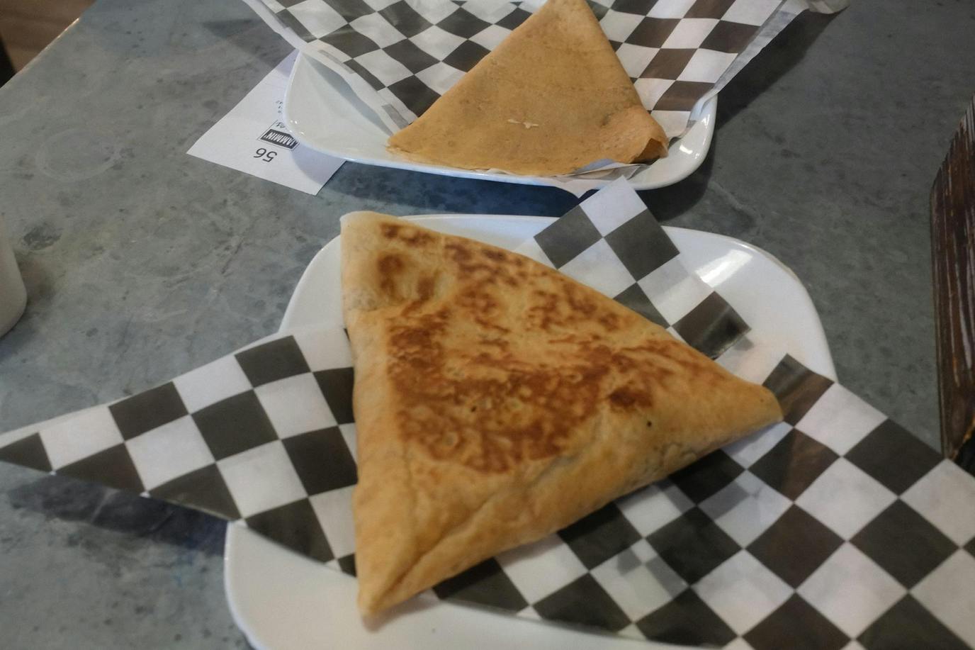 There are two white plates and both have a black and white checkered paper lining. There is one brown triangle shaped crepe on each plate. The plates sit on a light gray table.