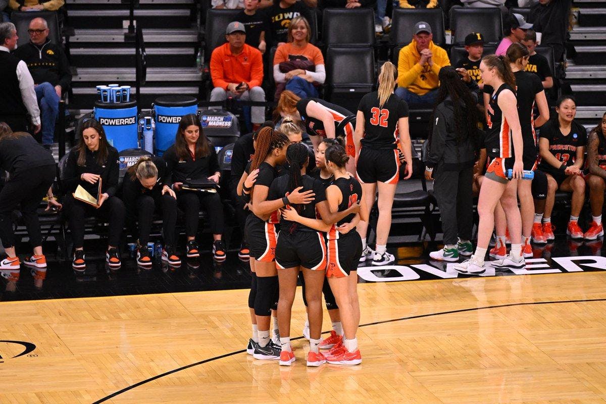 A group of women in black jerseys huddle on basketball court.