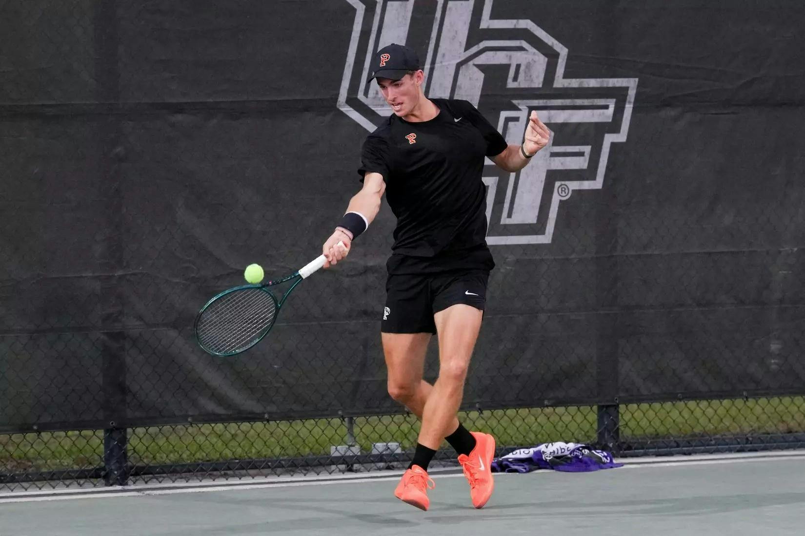 A tennis player wearing an all-black Princeton uniform hits a forehand on an outdoor hard court.