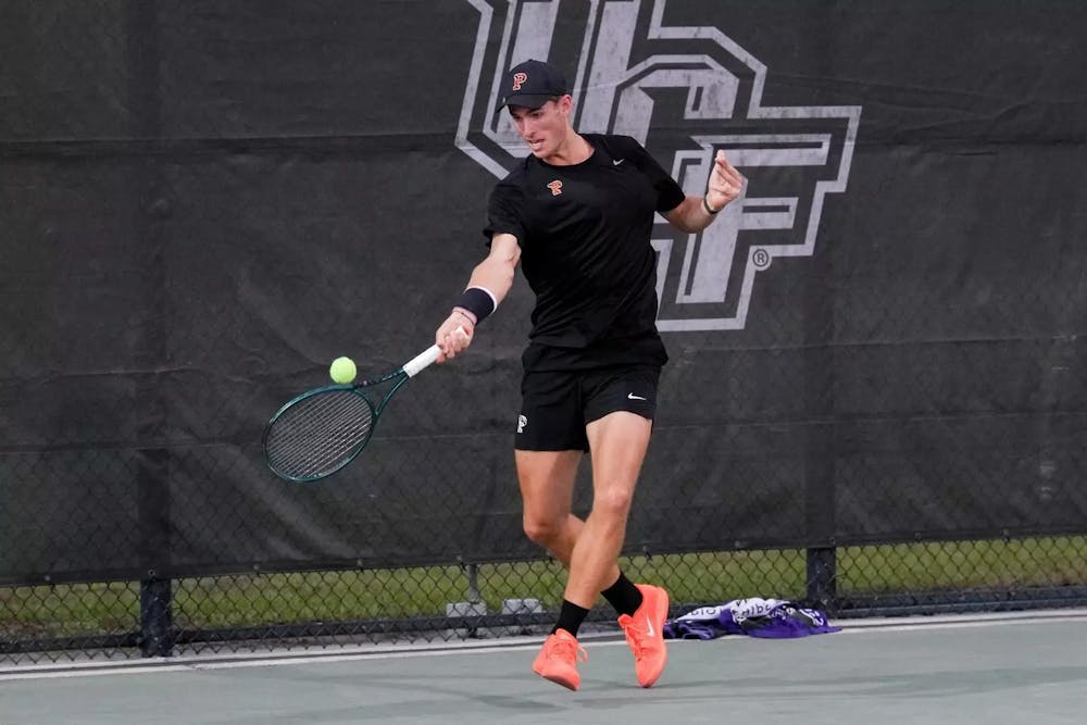 A tennis player wearing an all-black Princeton uniform hits a forehand on an outdoor hard court.