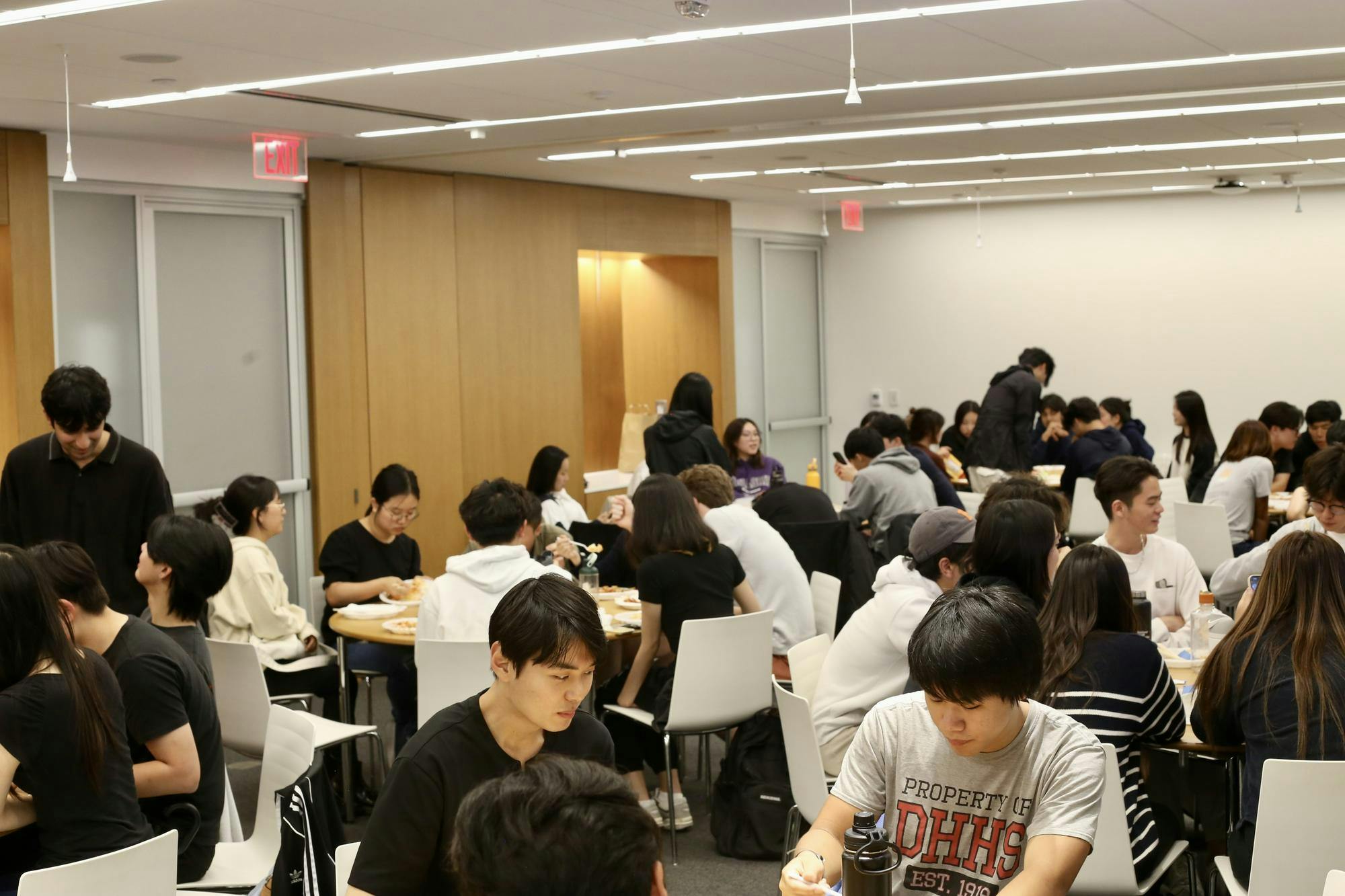 Students are sitting by several round tables eating Korean food. 